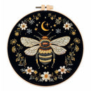 An embroidery hoop featuring a detailed stitched design of a bumblebee, a crescent moon, stars, and white flowers on a black background.