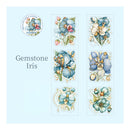 A sheet of floral stickers featuring blue and white irises with pink accents, labeled 'Gemstone Iris' on a light blue background. A circular logo for 'Gems of Life & Flower' is visible in the top left.