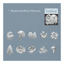 A product display card for 'Shattered Silver Flowers' by The Silver Craze, featuring ten metallic silver flower and mushroom charms arranged on a slate blue background, with a small product box in the upper right corner.