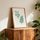 Framed artwork with green plant design on a wooden cabinet against a light wall.