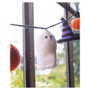 A white crocheted ghost ornament hanging on a string between window panes, with a purple witch hat and orange pumpkin partially visible in the background.
