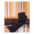 A person's hand wearing a black cable-knit fingerless glove or wrist sleeve, reaching toward books on a wooden bookshelf.