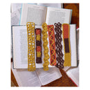 Five handmade crochet book spacers in mustard yellow, brown, orange, and red patterns, arranged on top of open books.