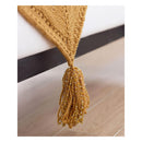 A close-up of a mustard yellow knitted textile with a tassel, draped over a dark horizontal bar against a light background and wood floor.