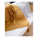 A mustard yellow knitted throw blanket with an intricate floral lace pattern and a tassel, draped over a white sofa next to light gray pillows.