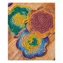 Three handmade crocheted flower-shaped coasters in earthy multicolor patterns, displayed on a wooden tabletop.