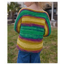 A child wearing a colorful striped knit sweater, shown from the back in an outdoor setting with grass and a house in the background.