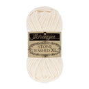 A skein of Scheepjes Stone Washed XL yarn in a warm cream color, wrapped with a black and beige paper label, on a solid white background.