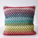 A square crocheted throw pillow with a colorful gradient pattern of red, orange, yellow, green, blue, and purple, set against a plain white background.