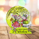 A festive round Christmas card or plaque featuring two illustrated mice holding ornaments, with the text 'CHRISTMAS Whiskers' on a bright yellow-green base, photographed on a wooden surface against a blurred holiday bokeh background.