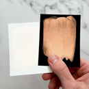 Hand holding a swatch of beige makeup against a marble background