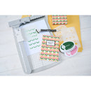 Crafting tools and materials including a paper cutter, stamps, and patterned paper on a white surface.