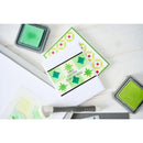 Card with green stamping design on a white surface with stamps and ink pads.