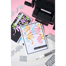 Card with colorful wavy text and 'happy birthday' on a pink background with cutting dies and tools.