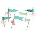 Six decorative paper flag picks arranged on a plain white background. The flags are mostly light aqua and pale mint green, with some pink ribbon accents and wooden sticks.
