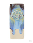 A rectangular ceramic tile or coaster featuring a blue and yellow marbled glaze with a white embossed lotus flower design in the center, set against a plain white background.