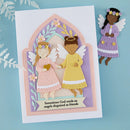 A handmade layered paper card featuring two angel figures, one in pink and one in yellow, with the text 'Sometimes God sends us angels disguised as friends'. A smaller matching angel cutout is placed to the right on a light blue background with decorative white leaves.