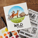 Card with animal illustration and 'Wild at Heart' text on a wooden surface with watercolor swatches and stamps.