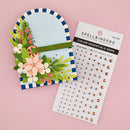 Spellbinders Color Essentials Gems rose gold adhesive gems shown on their white backing card next to a decorated arch card demonstrating their use, set against a solid pink background.