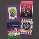 Four Halloween greeting cards arranged on a dark gray background. The cards feature whimsical designs: one with a pumpkin-headed figure, one with dancing skeletons, one with ghosts and a pumpkin, and one with a witch and owl on a diamond-patterned background.