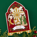 A decorative paper-cut style Christmas nativity sign featuring Mary, Joseph, baby Jesus, and a dove, with the text 'Glory to God Grace to You' on a green background with holiday greenery and red ornaments.