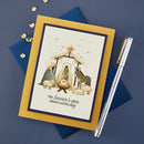 A personalized Christmas greeting card featuring a nativity scene with the text 'The Savior's Birth Brings Lasting Joy', styled on a navy blue envelope with a silver pen and gold confetti on a dark blue background.