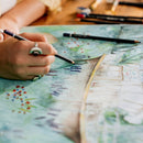 Person coloring a detailed illustration with colored pencils on a map.