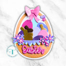 Colorful Easter egg-shaped card with bunnies, flowers, and a pink bow on a marble background.