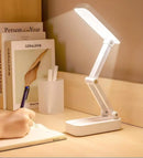 White desk lamp on a wooden surface with books and a pen holder in the background