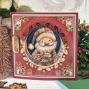 A square Christmas greeting card featuring a festive red background with a central circular illustration of Santa Claus surrounded by holly and gold decorative elements. The card is styled on a tabletop with holiday decorations, including a miniature tree and greenery.