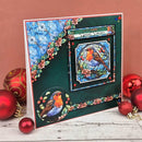 A handmade Christmas card featuring robin birds in stained-glass style, displayed on a rustic white wooden surface with red Christmas ornaments against a terracotta background.