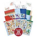 A set of Christmas-themed craft paper sheets and stickers displayed in a fan arrangement on a white background, with a red circular badge at the bottom that reads 'INCLUDES 20 SHEETS'. The sheets feature festive illustrations of gnomes, Santa Claus, snow scenes, and holiday patterns in blue, red, green, beige, and white.