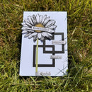 Card with a black and white flower illustration and text on grass