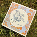 Card with floral illustration and 'Fuschia' text on decorative background, placed on grass.