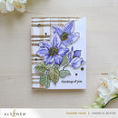 Card with purple flowers and 'thinking of you' text on a wooden surface with white flowers.