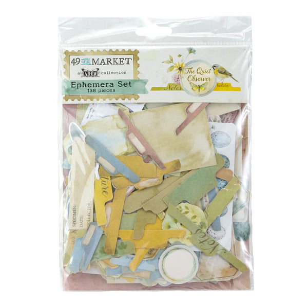 A packaged scrapbook ephemera set from 49th Market Kits, containing 158 pieces. The clear plastic bag shows a variety of paper cutouts in muted pastel colors including yellow, green, blue, and beige, along with small labels and decorative pieces.