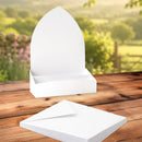 White display stand and matching sheets of cardstock or paper placed on a wooden table, with a blurred outdoor garden background.