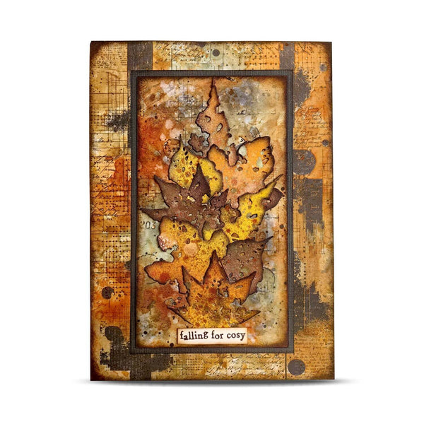 A square decorative art piece featuring layered autumn maple leaves in orange, yellow, and brown tones over a distressed vintage-style background with script and texture. The piece has a dark border and a small label at the bottom reading 'falling for cosy'.