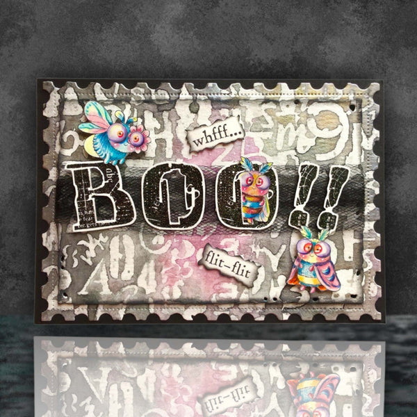A square mixed-media art card featuring the word 'BOO!!' in large distressed black letters, decorated with colorful whimsical insect and bird illustrations, torn paper labels, and a gray serrated border, shown against a dark textured background with a reflection below.