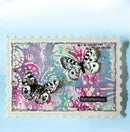 A square handmade greeting card with a scalloped white border, featuring two black-and-white spotted butterflies over a colorful abstract background in purple, pink, teal, and white. A small black label reads 'Satisfaction'.