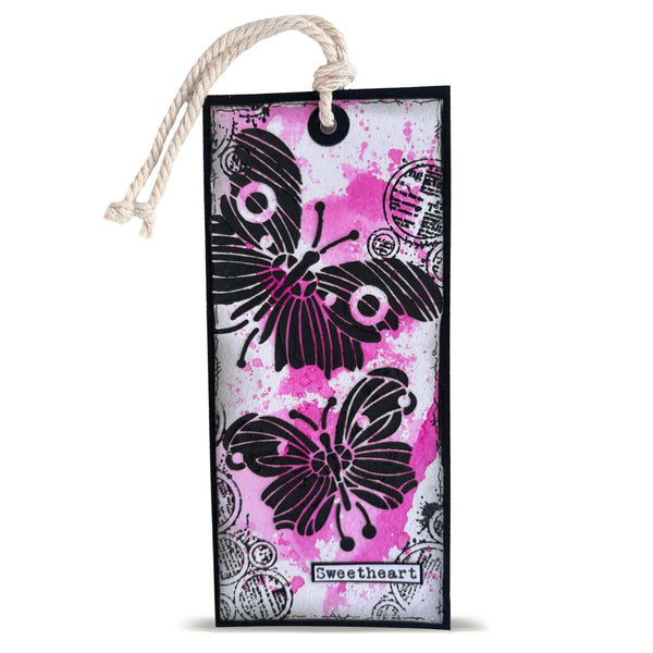 A rectangular paper bookmark or gift tag with a hanging rope loop, featuring black butterfly and floral stamp designs over a pink, white, and gray splattered background. The word 'sweetheart' is printed at the bottom.