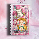 A spiral-bound mixed-media art journal featuring a whimsical chibi-style illustration of a blonde girl holding a grapevine, surrounded by pink watercolor splashes, collage paper textures, and the quote 'every stitch tells a story'.