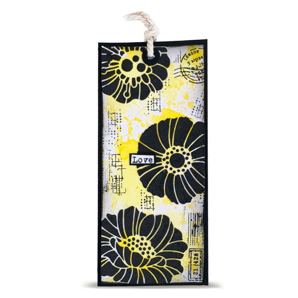 A rectangular decorative bookmark or art tag with a white hanging string, featuring large black floral silhouettes, yellow splatter accents, and mixed printed text and line details on a white background.