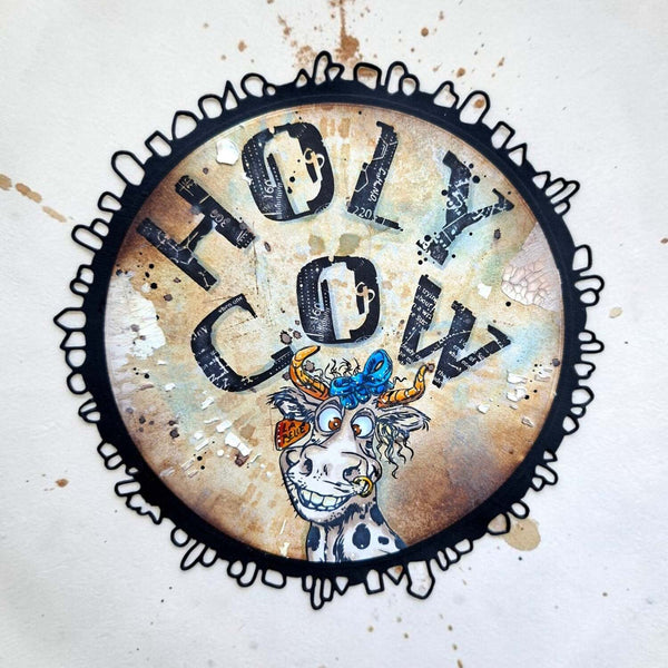 A circular art print or sticker featuring a stylized cow illustration and the text 'HOLY COW' in large distressed letters, centered on a white background with paint splatter details.