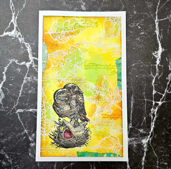 A framed art print featuring a detailed illustration of an owl perched on a nest, set against a vibrant yellow and green watercolor background with faint script and leaf patterns. The print is displayed on a dark gray marble surface.