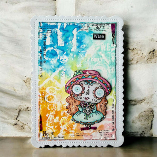 A square mixed-media art card featuring a colorful sugar skull illustration, displayed against a textured, light-colored stone wall background.