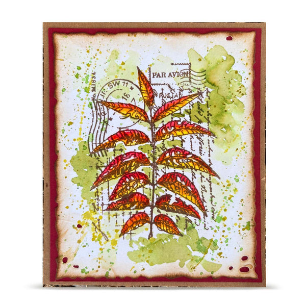 A square handmade art card featuring a central illustration of red and orange autumn leaves over a distressed white background with green watercolor splashes, postage stamp details, and a reddish-brown border.