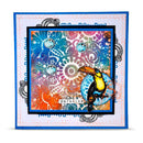 A square handmade-style art card or print featuring a colorful abstract mandala and swirl pattern in blue, pink, orange, purple, and teal, with a toucan illustration on the lower right and the word "paradise" near the bottom. The artwork is layered over a white dotted border with blue decorative text and ornamental flourishes, shown against a light gray background.
