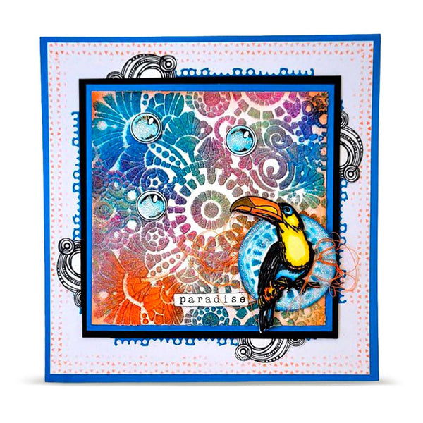 A square handmade-style art card or print featuring a colorful abstract mandala and swirl pattern in blue, pink, orange, purple, and teal, with a toucan illustration on the lower right and the word "paradise" near the bottom. The artwork is layered over a white dotted border with blue decorative text and ornamental flourishes, shown against a light gray background.
