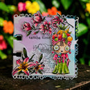 A colorful handmade art card with a scalloped white border, featuring illustrated flowers, a stylized woman in a green dress, and the text 'samba time', photographed outdoors against a blurred background of green foliage and flowers.